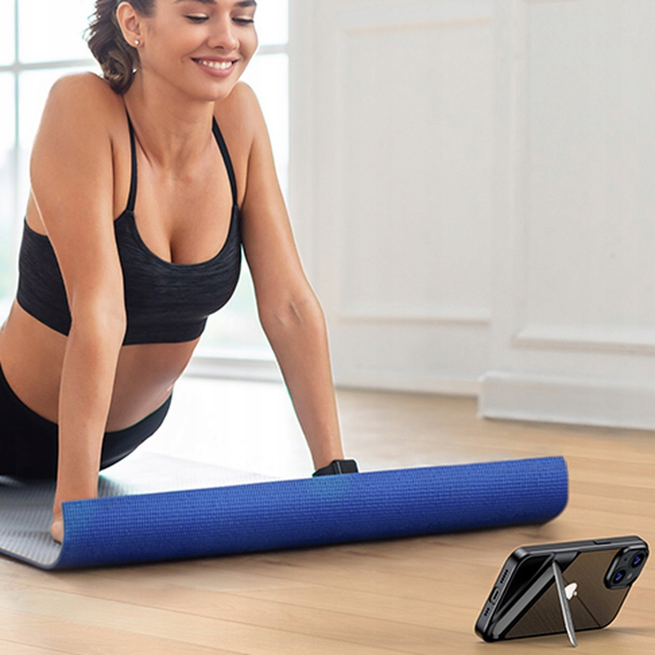 Una donna fa yoga con un telefono appoggiato in una custodia. Un tappetino da yoga blu è sullo sfondo.