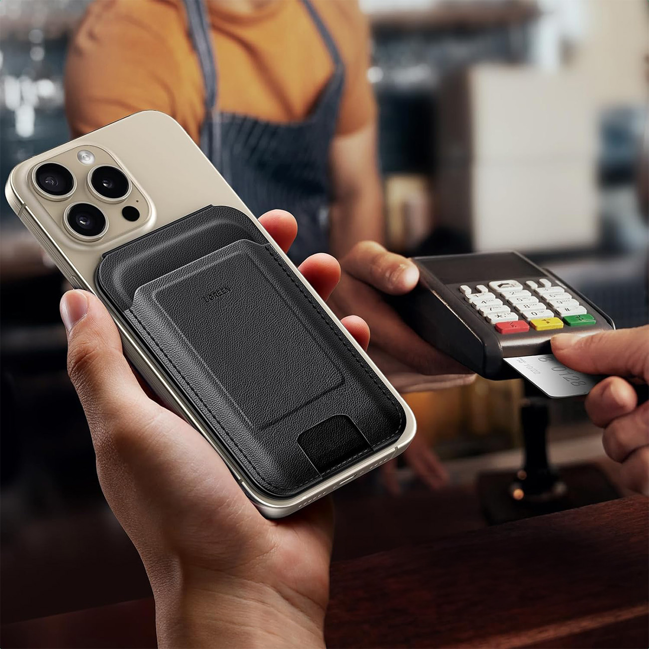 Osoba trzymająca telefon z dołączonym portfelem, płacąca kartą kredytową przy ladzie.