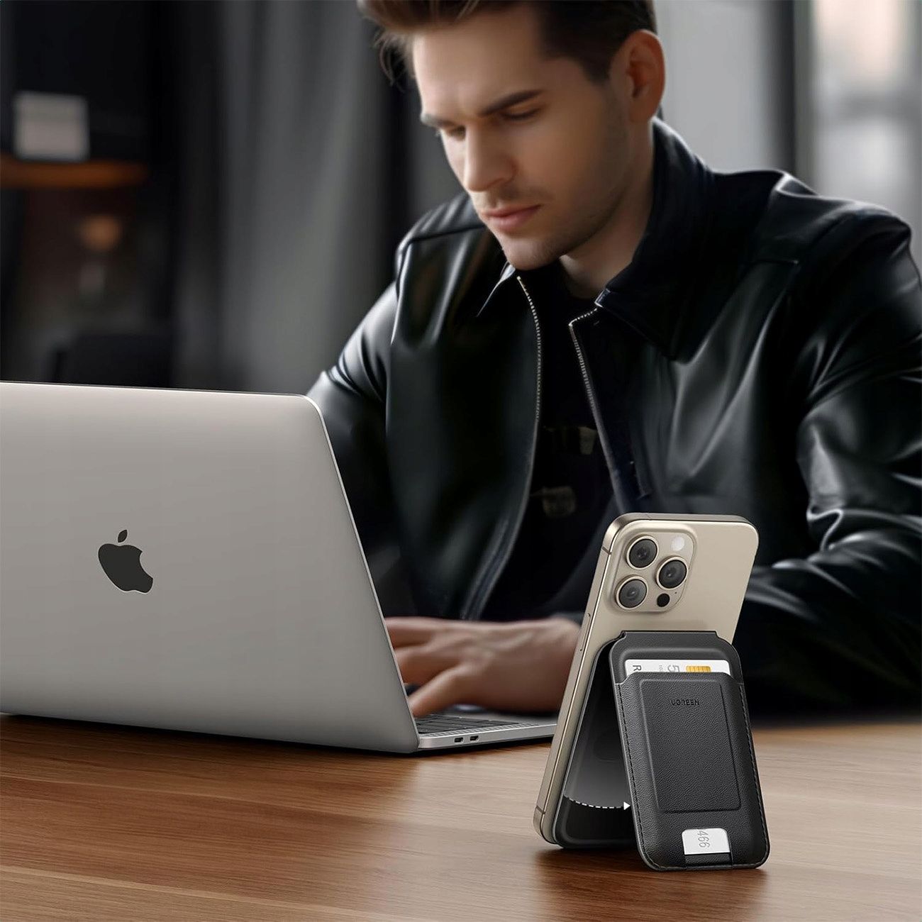 Mężczyzna używający laptopa i telefonu z dołączonym portfelem, siedzący przy oknie, poważna mina.