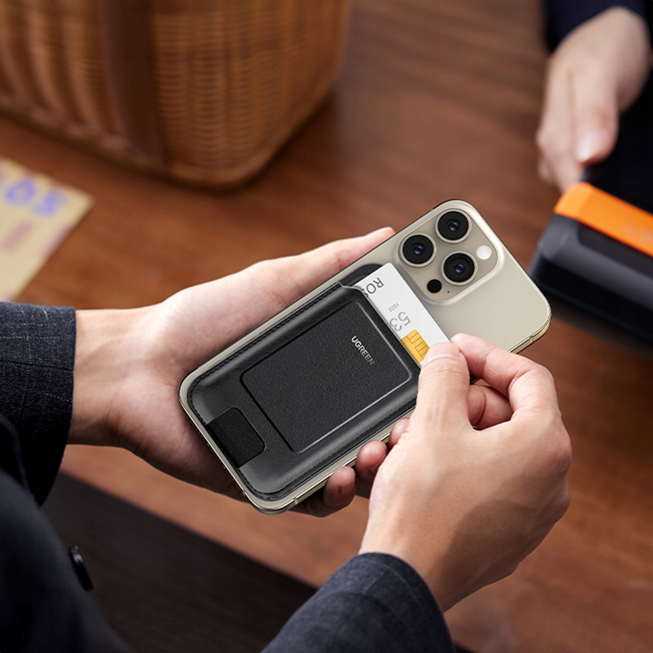 Dłonie trzymające telefon z dołączonym portfelem, inna osoba używa czytnika kart.