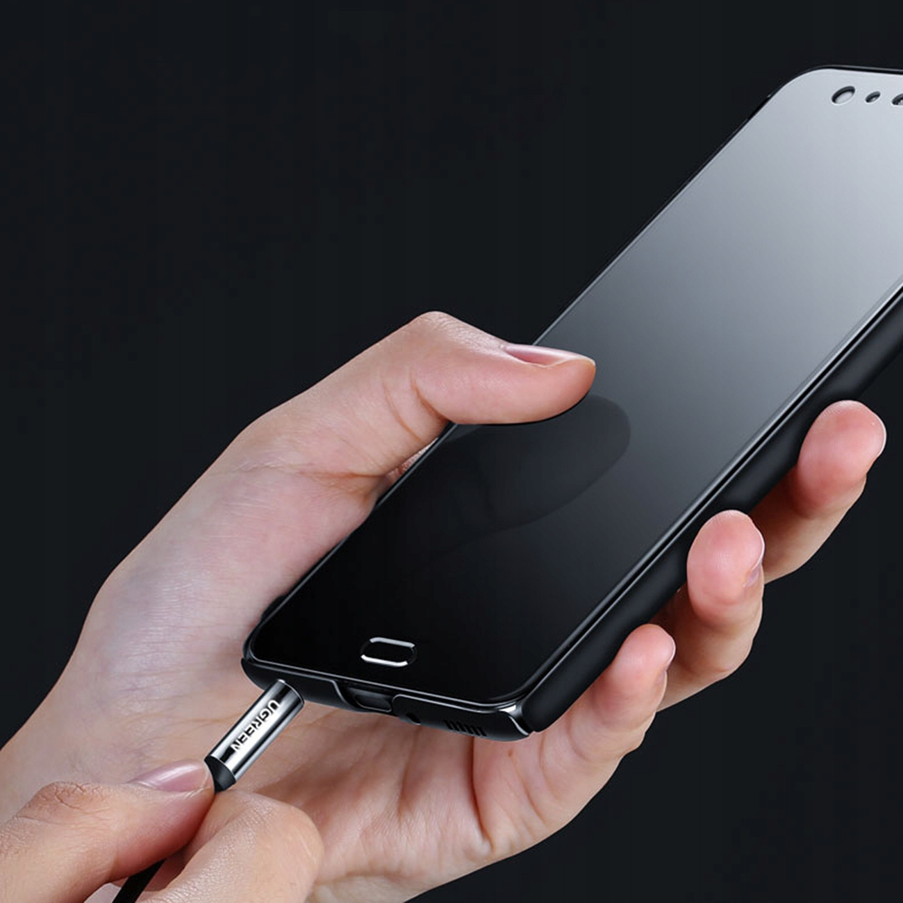 Dłoń wkładająca złącze jack do czarnego smartfona. Czarne tło.