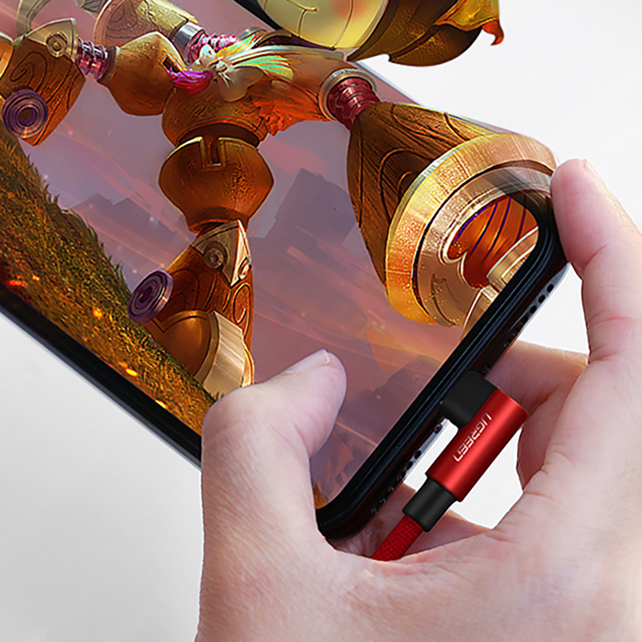 Ręka trzyma telefon z grą na ekranie, podłączony do czerwonego kabla z wtyczką UGREEN.