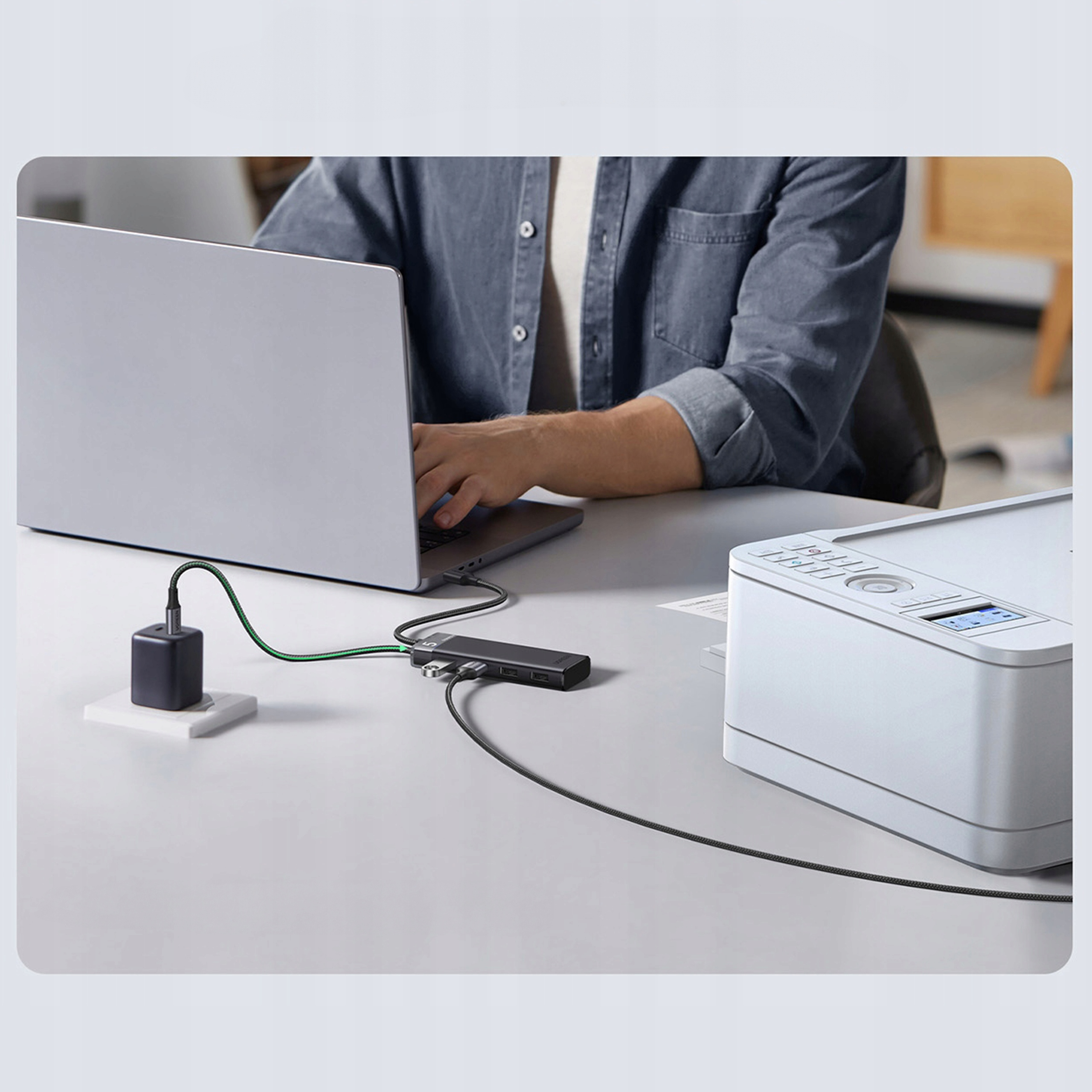 Osoba pracująca na laptopie podłączonym do huba i drukarki na biurku.