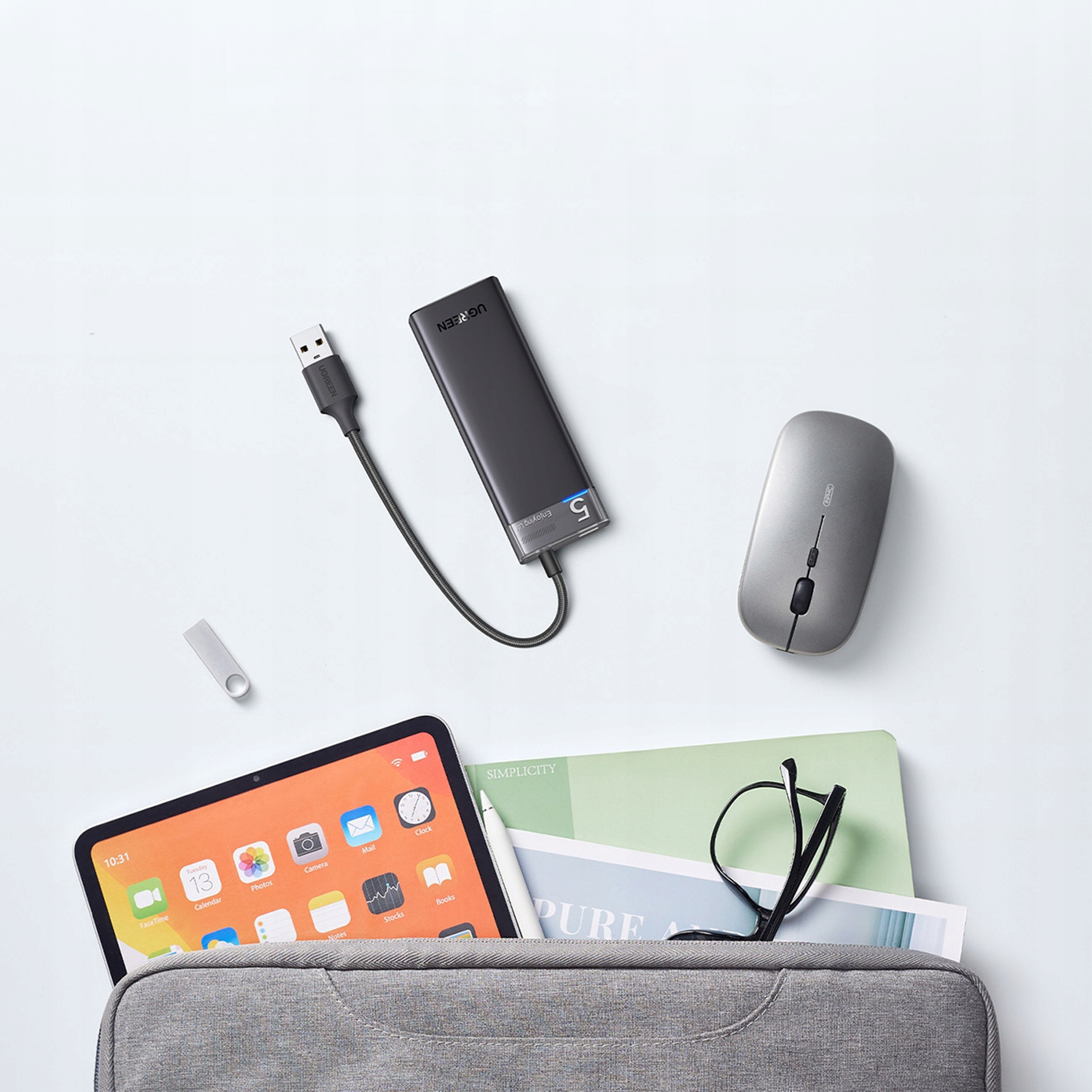 Tablet, mysz, hub i inne przedmioty w szarej torbie na białej powierzchni.