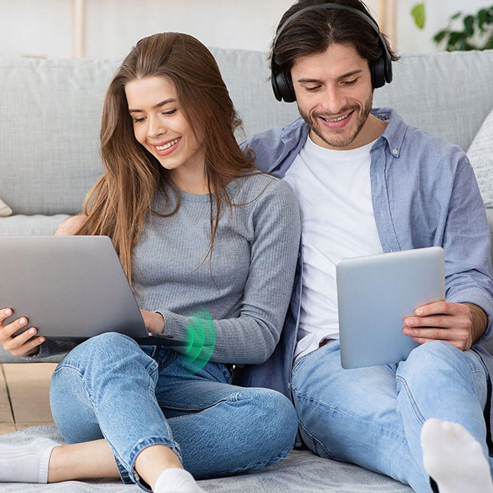 Mężczyzna i kobieta uśmiechają się. Siedzą na podłodze, używając laptopa i tabletu.
