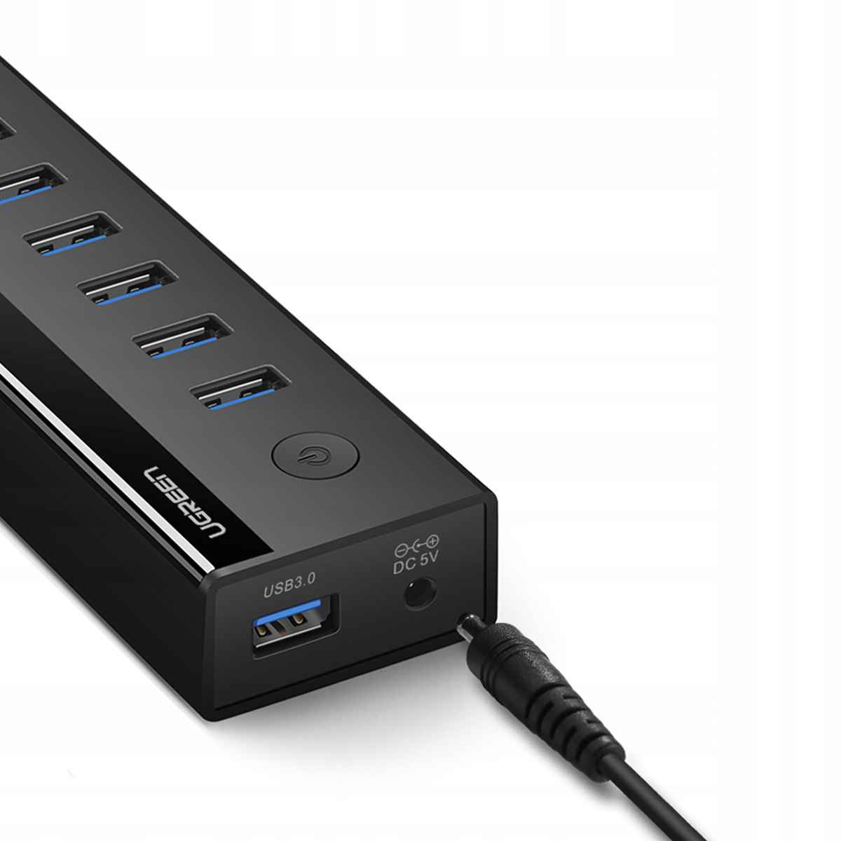 Nahaufnahme eines schwarzen UGREEN USB-Hubs mit mehreren USB-Anschlüssen. Ein Netzkabel ist an der Seite des Hubs angeschlossen.