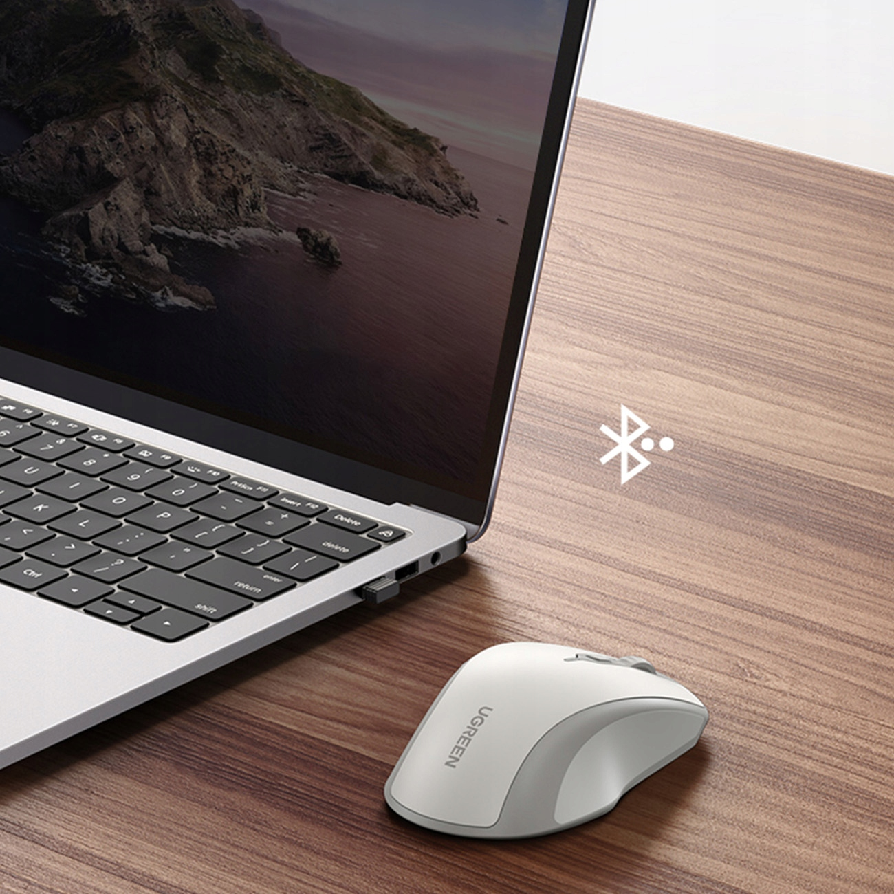 Biała mysz UGREEN obok laptopa. Symbol bluetooth jest pokazany na drewnianej powierzchni.