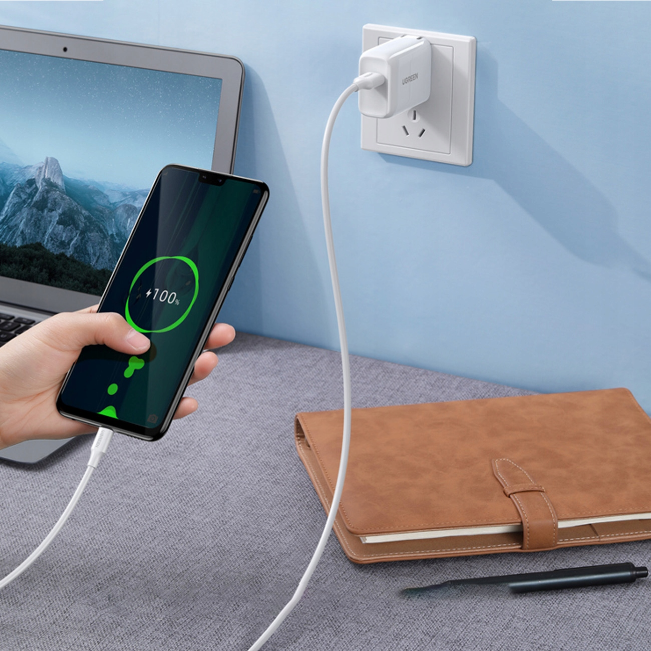 Telefon ładujący się kablem i ładowarką UGREEN, na biurku z notatnikiem.