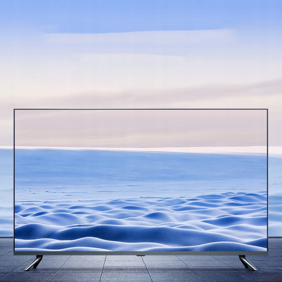 Telewizor z dużym ekranem wyświetlający ośnieżony krajobraz, umieszczony na tle nieba, na kafelkowej powierzchni.