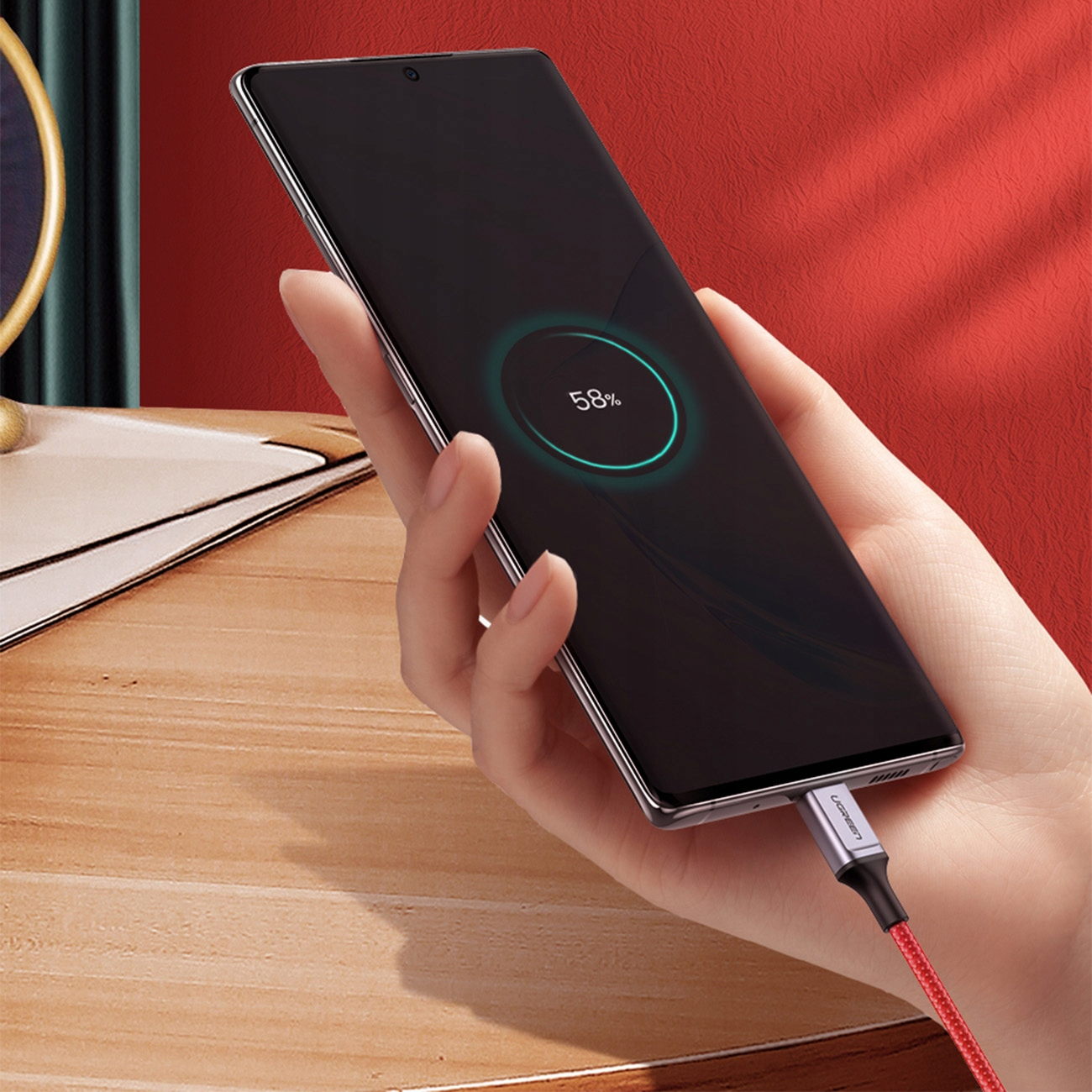 Ręka trzyma ładujący się telefon z podłączonym kablem USB-C. Telefon pokazuje stan naładowania 58%.