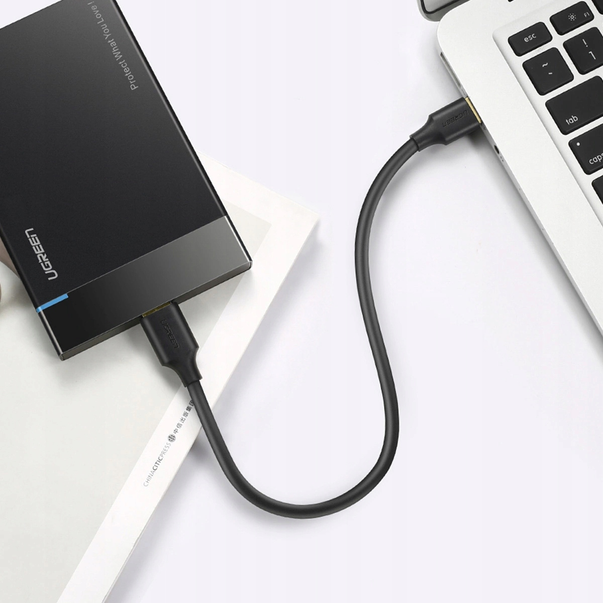Czarny kabel UGREEN łączy czarny zewnętrzny dysk twardy ze srebrnym laptopem. Laptop jest otwarty.