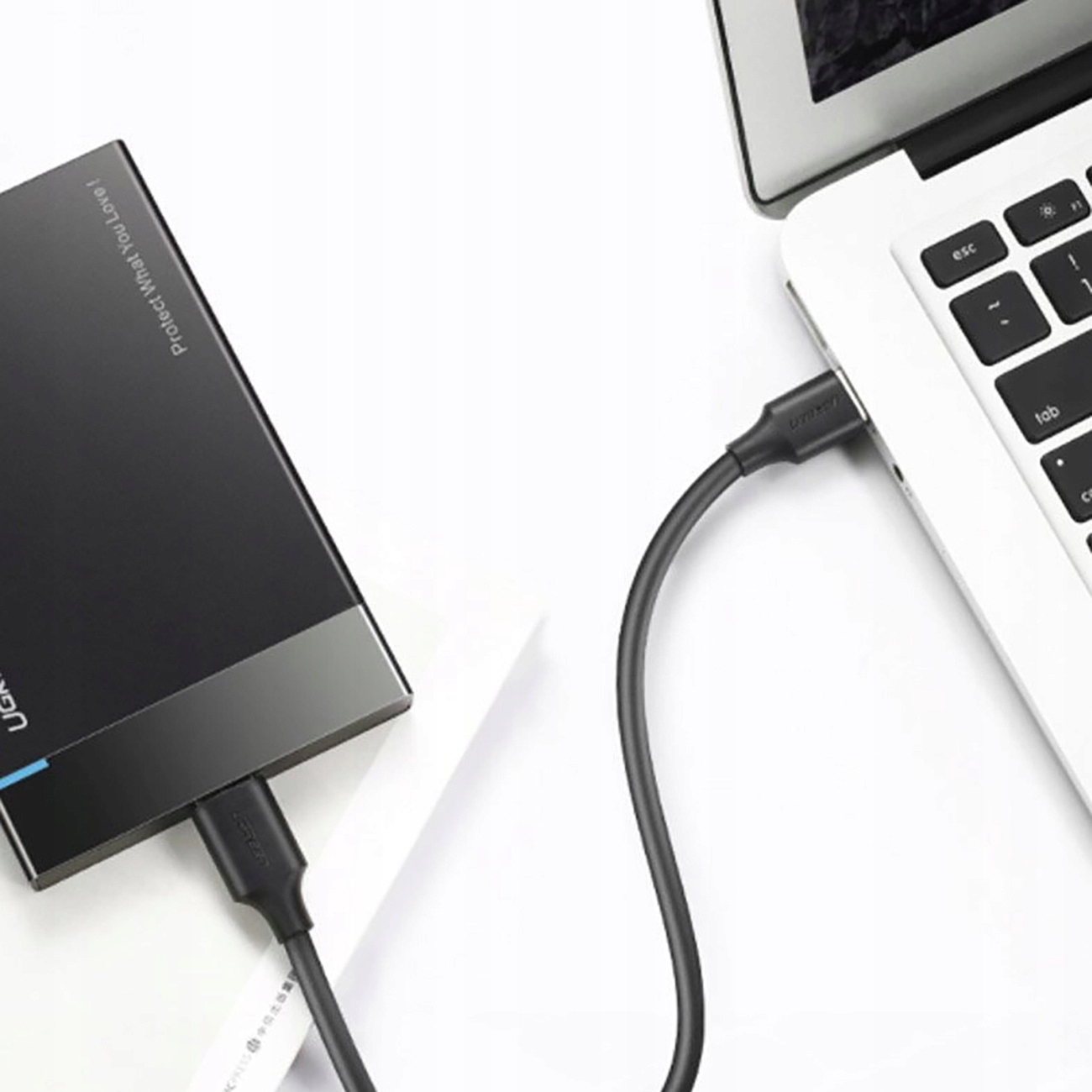 Un disco rigido esterno nero collegato a un laptop argento con un cavo UGREEN nero.