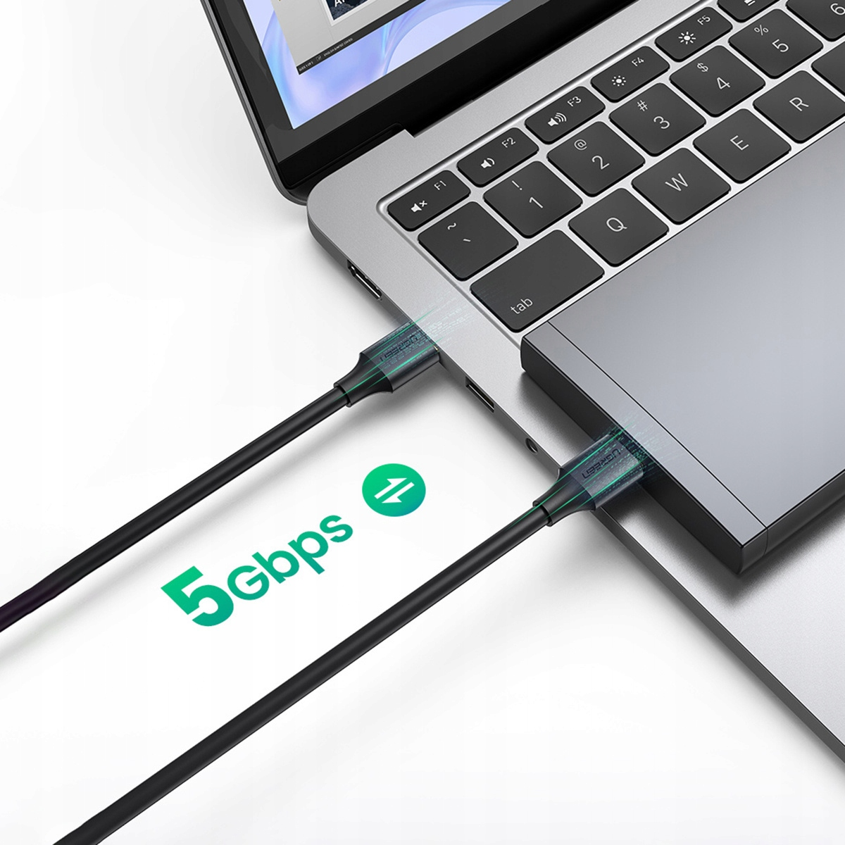 Laptop z podłączonymi kablami USB. Widoczne zielone logo 5 Gbps. Laptop jest srebrny, a kable czarne.