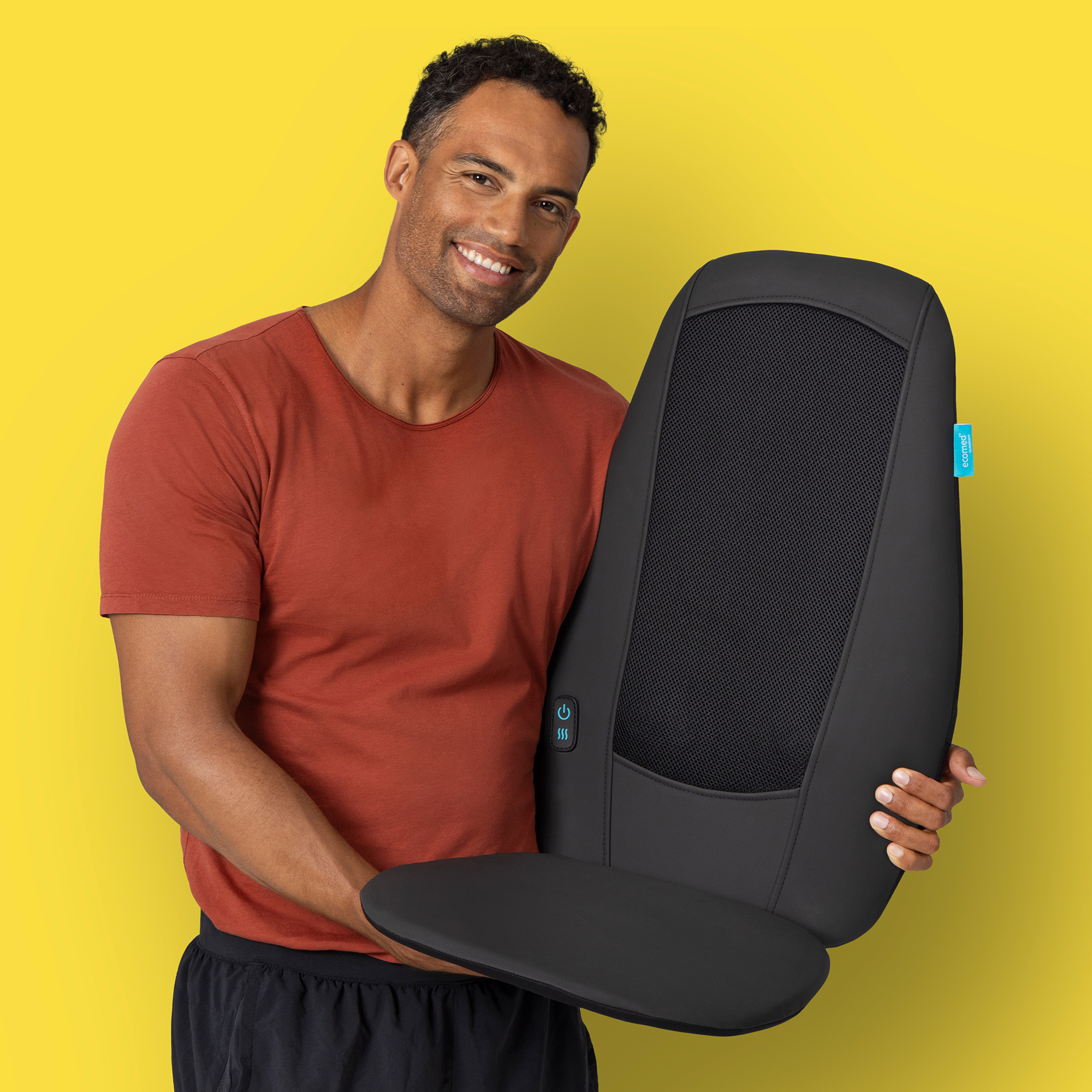 Mężczyzna trzyma czarne urządzenie do masażu, uśmiecha się do kamery, na żółtym tle.