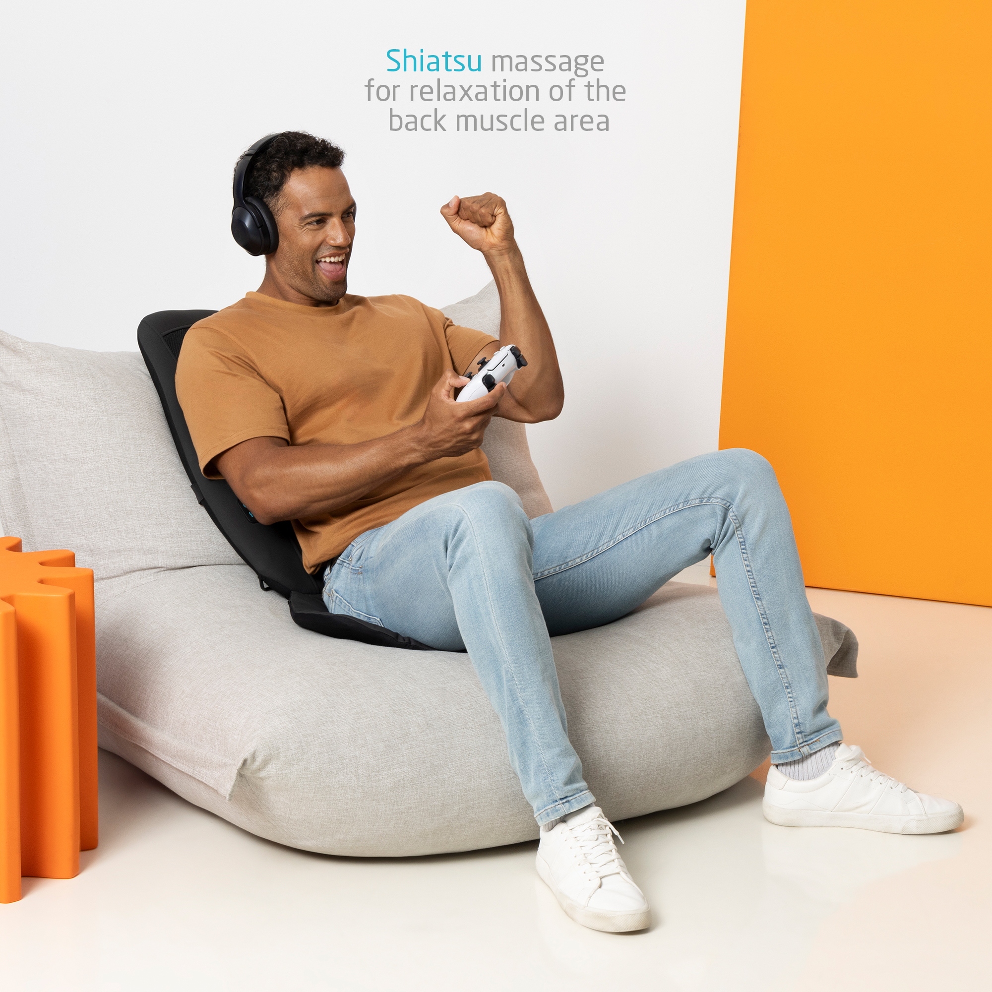 Mężczyzna siedzi na sofie, ma słuchawki i kontroler do gier, uśmiecha się.