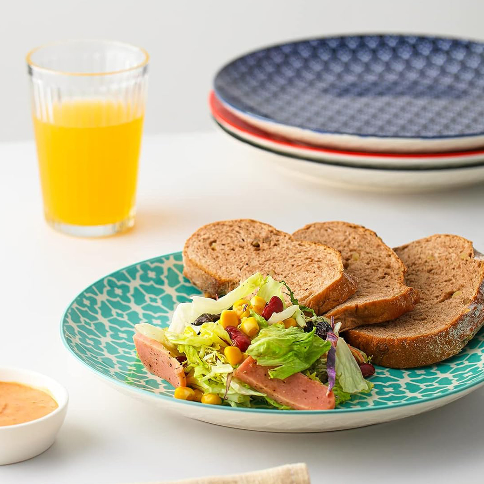 Ein Teller mit Salat und Brot, ein Glas Saft und zwei Teller im Hintergrund.