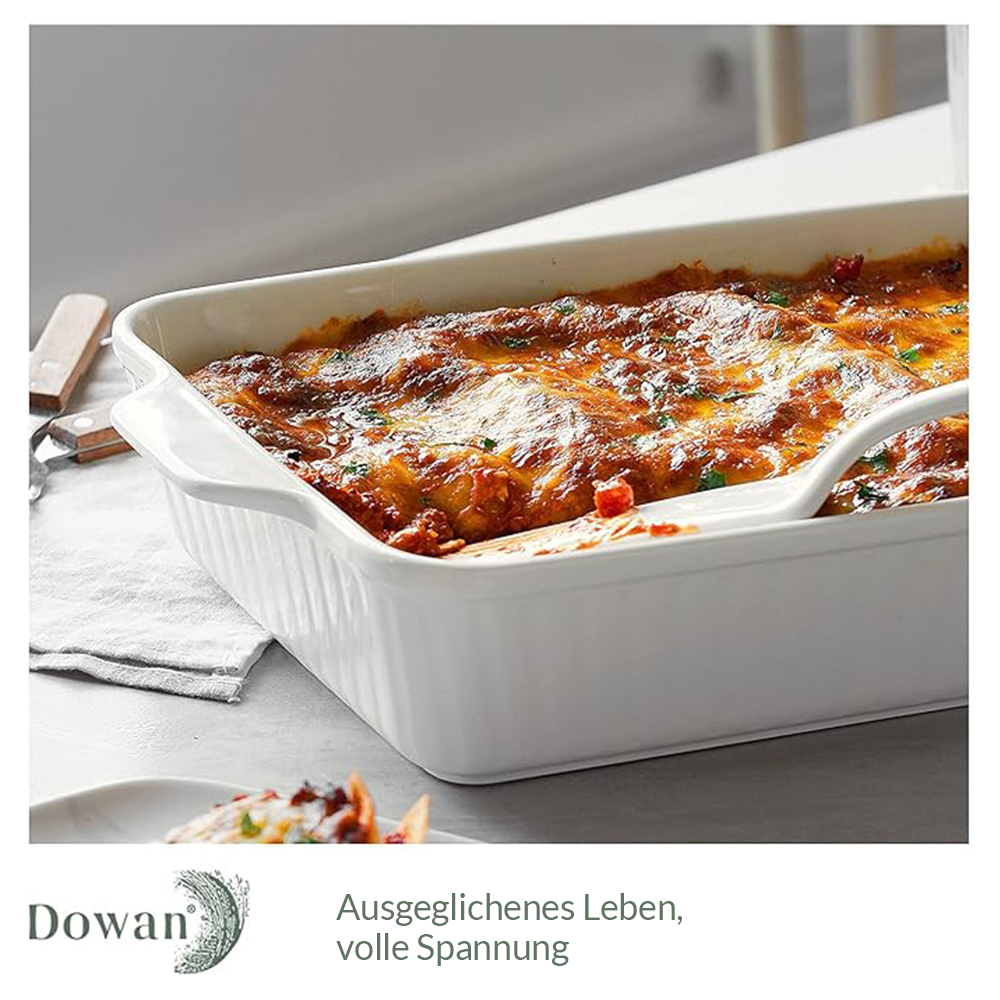 Una pirofila rettangolare bianca con lasagne. Un cucchiaio bianco poggia sulla pirofila. Un tavolo bianco.