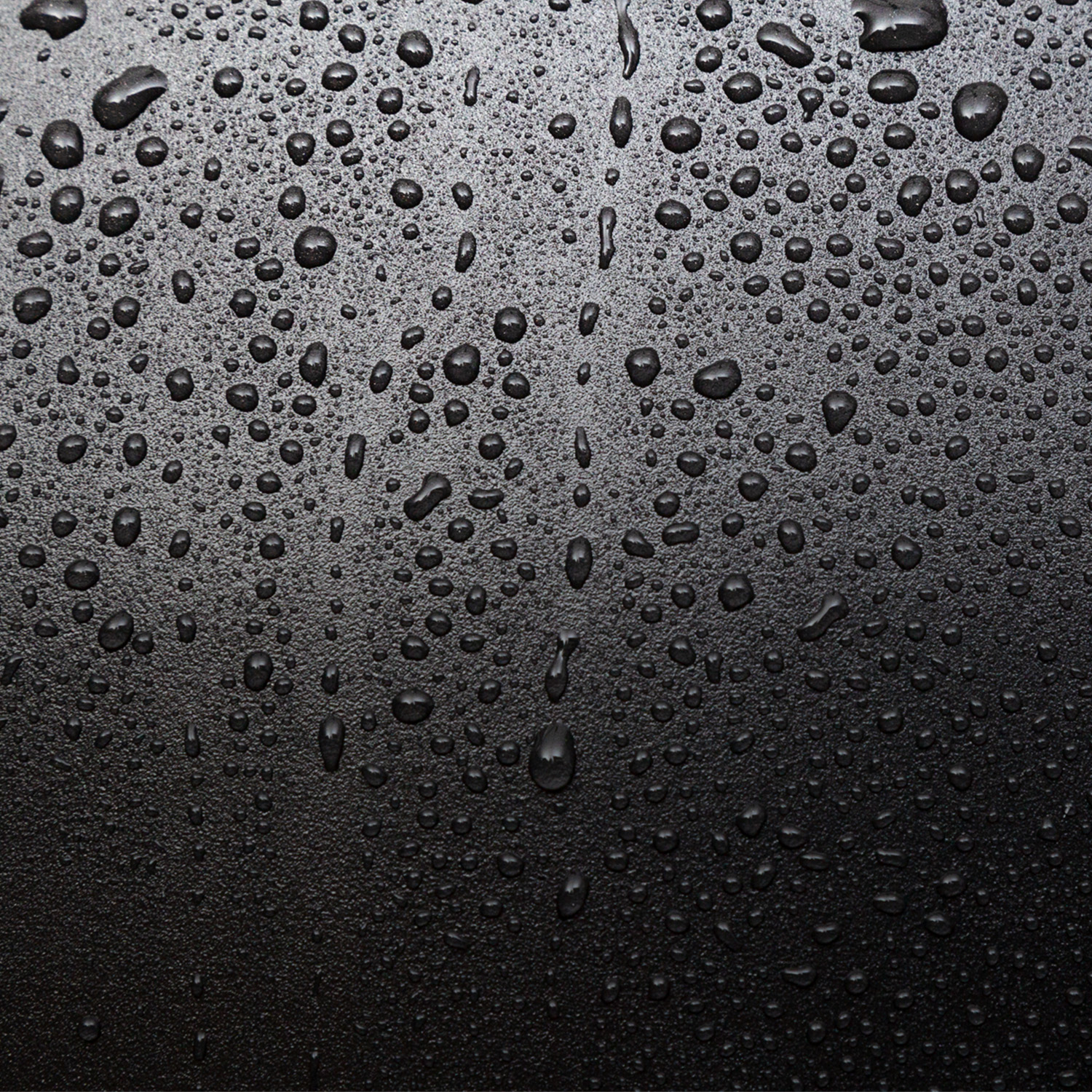 Nahaufnahme von Wassertropfen auf einer dunklen, strukturierten Oberfläche.