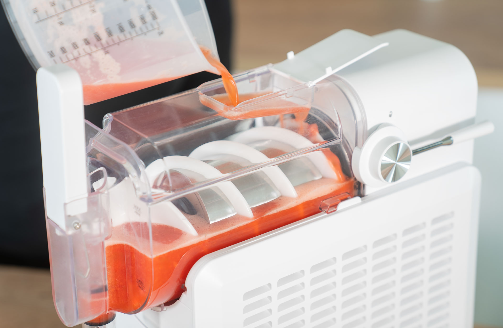 Biała maszyna jest napełniana różowym płynem z miarki, na białym tle.