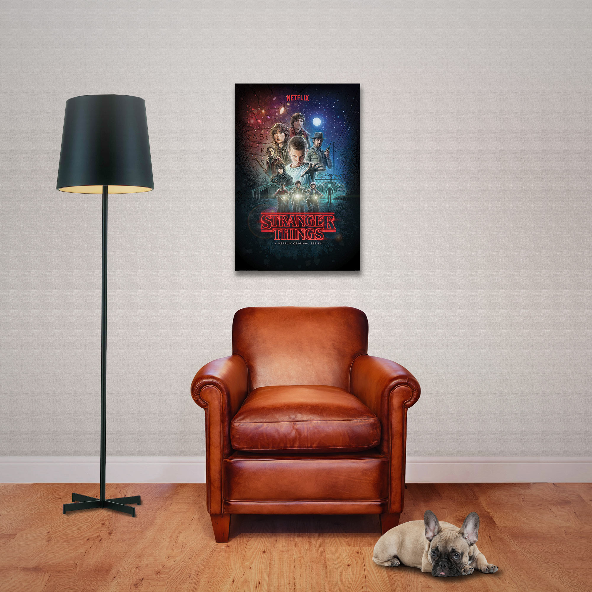 Ein Poster von Stranger Things hängt an der Wand neben einer Lampe und einem braunen Ledersessel. Ein Hund liegt am Boden.