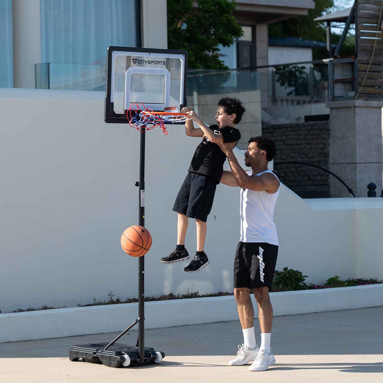 Un père et son fils jouent au basket. Le père aide son fils à atteindre le panier.