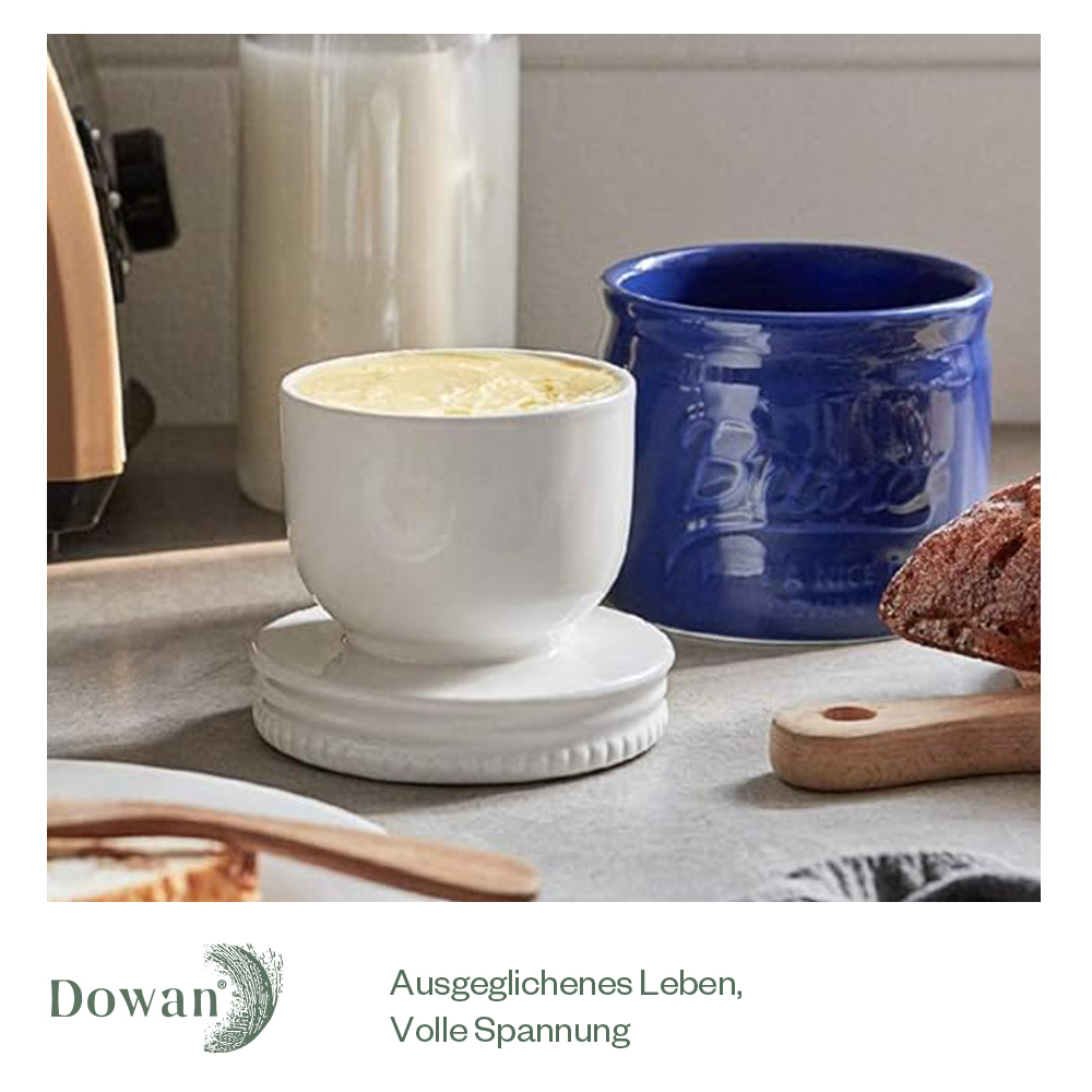 Weiße Butterdose mit Butter und eine blaue Butterdose. Weitere Artikel im Hintergrund.