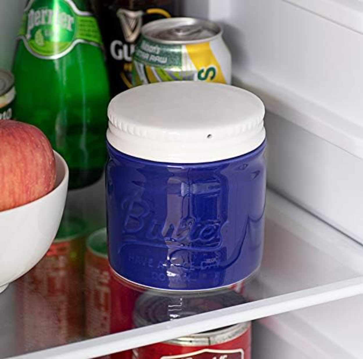 Ein blaues Butterglas mit weißem Deckel im Kühlschrank zwischen anderen Artikeln.
