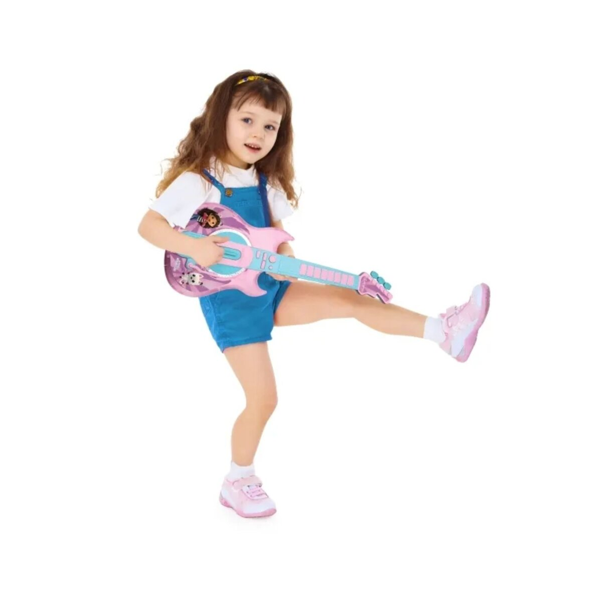 Ein junges Mädchen mit einer Gitarre. Sie trägt blaue Latzhosen und pinke Schuhe und spielt Gitarre.