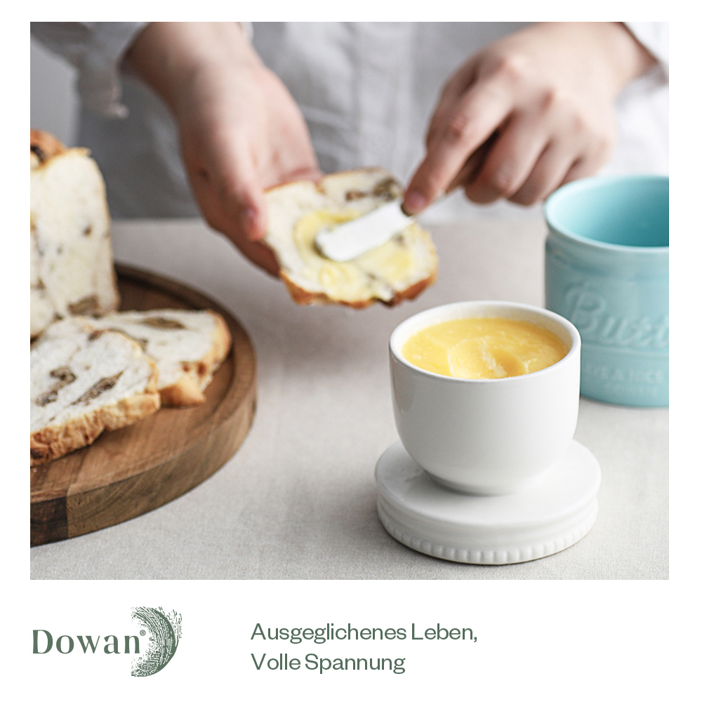 Eine Person bestreicht Brot mit Butter. Eine kleine weiße Butterdose im Vordergrund. Brot.