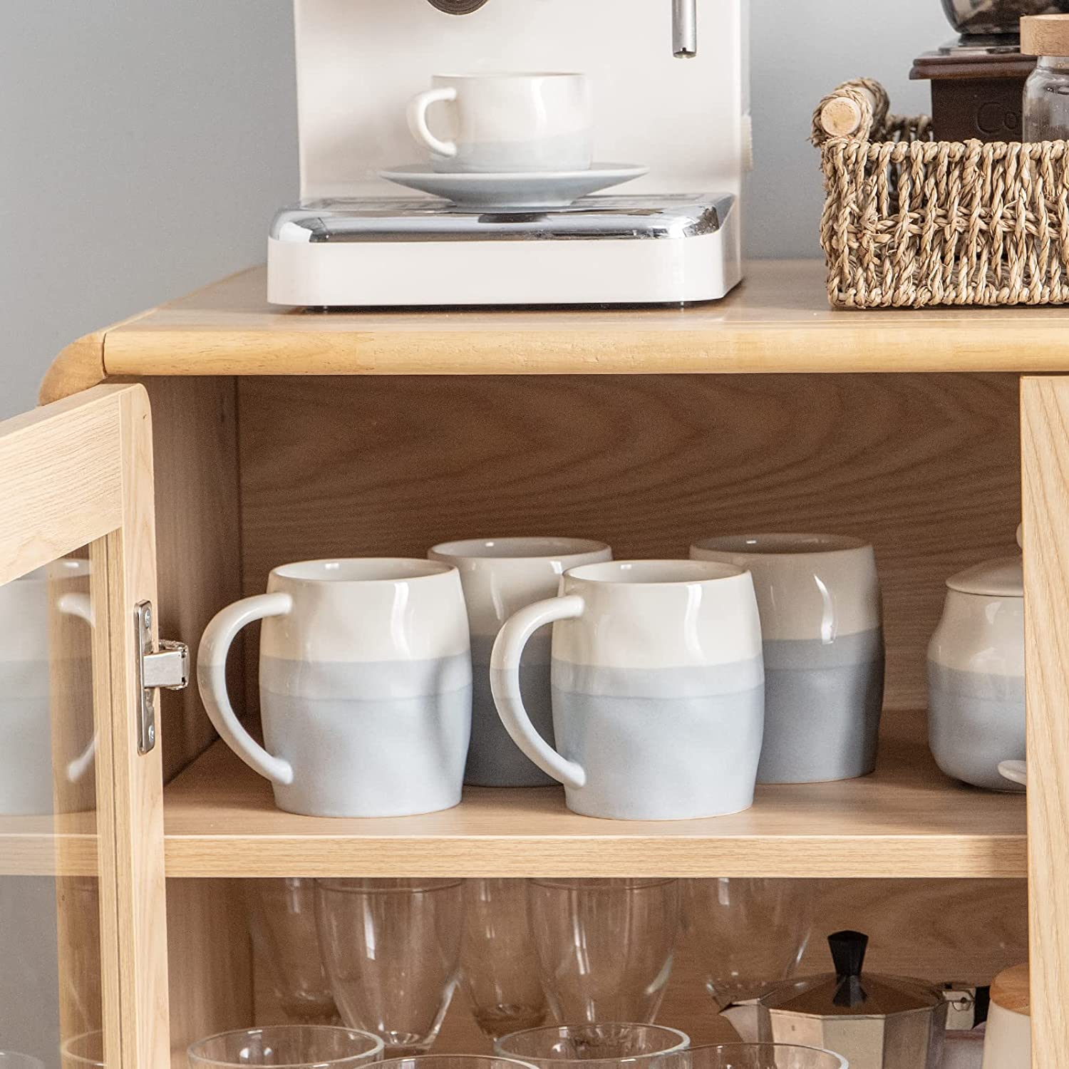 Mobile in legno con tazze, piattini e una macchina da caffè. Alcune tazze sono sul bancone e all'interno del mobile.