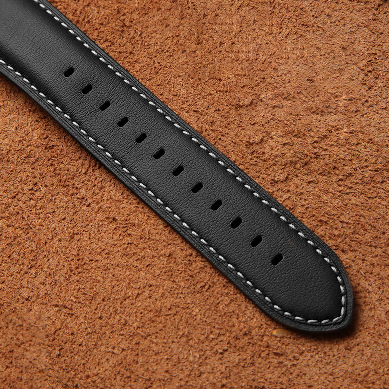 Schwarzes Lederarmband mit weißen Nähten auf brauner Lederoberfläche.
