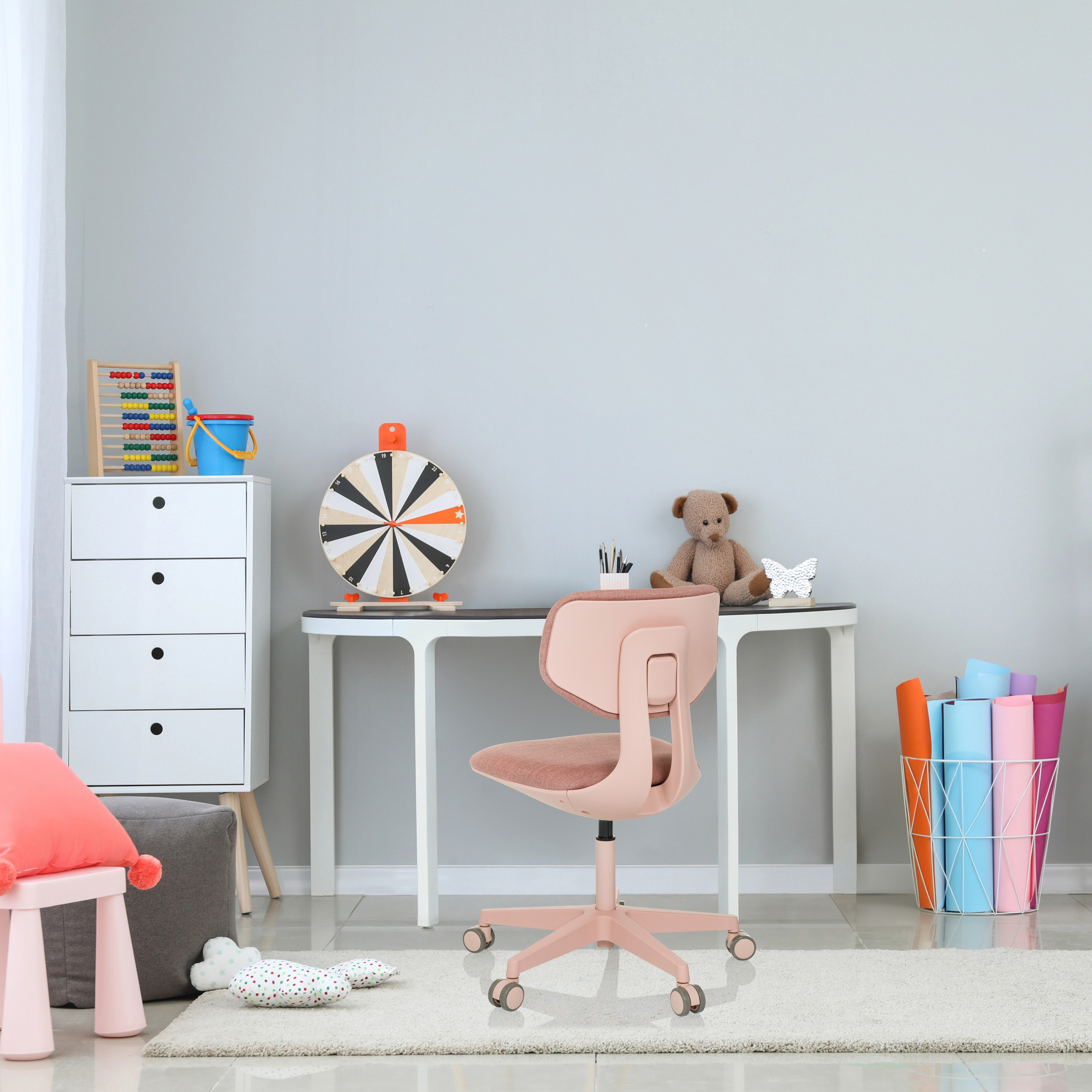 Ein rosafarbener Stuhl in einem Kinderzimmer. Das Zimmer hat einen Schreibtisch, Spielzeug und einen Teppich.