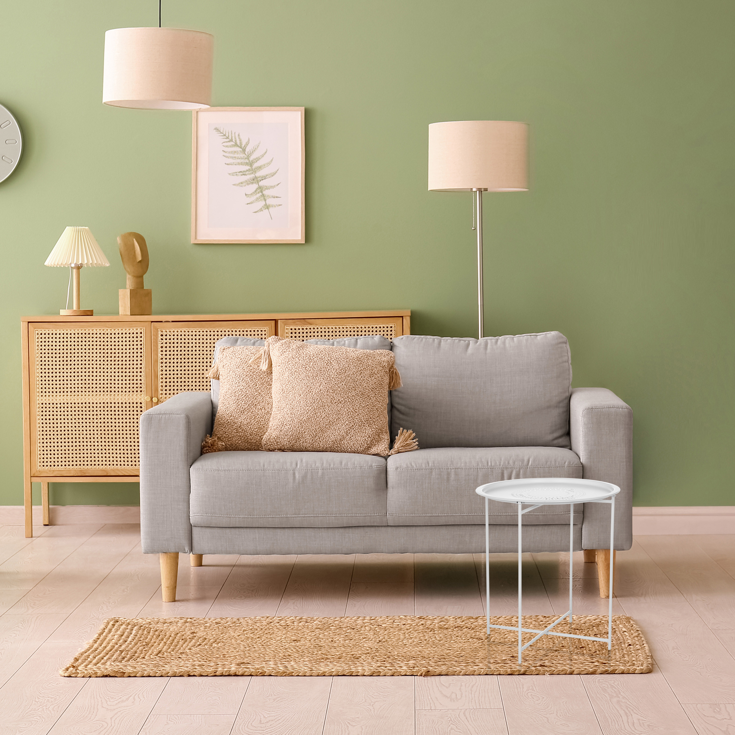 Ein Wohnzimmer mit grauem Sofa, weißem Beistelltisch, Teppich und Lampen vor einer grünen Wand.