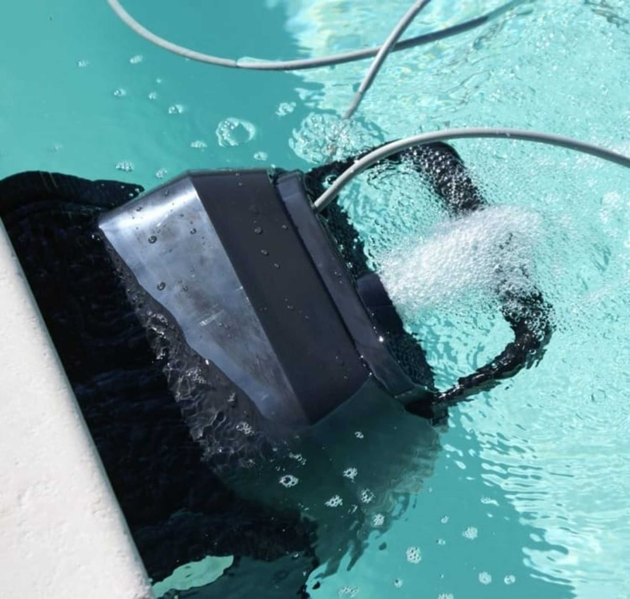 Un limpiador de piscina robótico sumergido en agua, con una manguera y burbujas visibles.