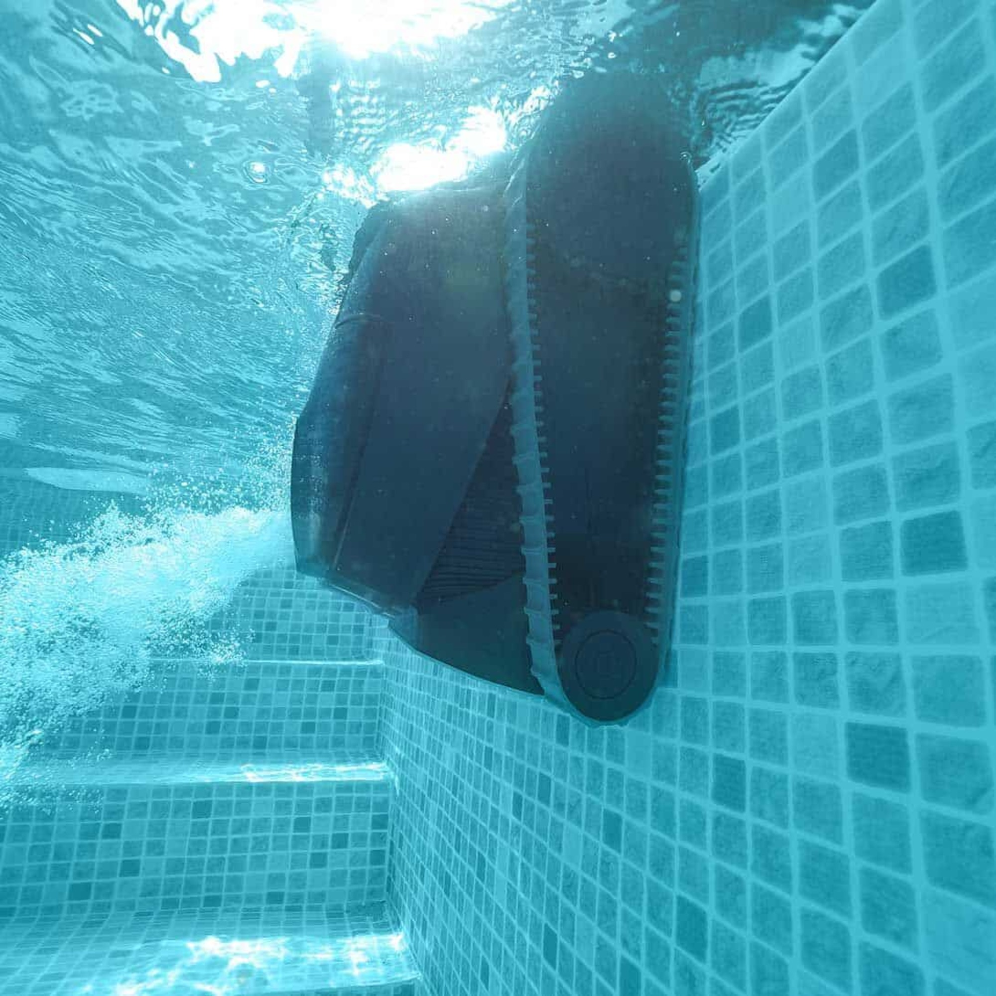 Toma submarina de un robot limpiador de piscinas. El robot es blanco y negro y limpia las baldosas de la piscina.