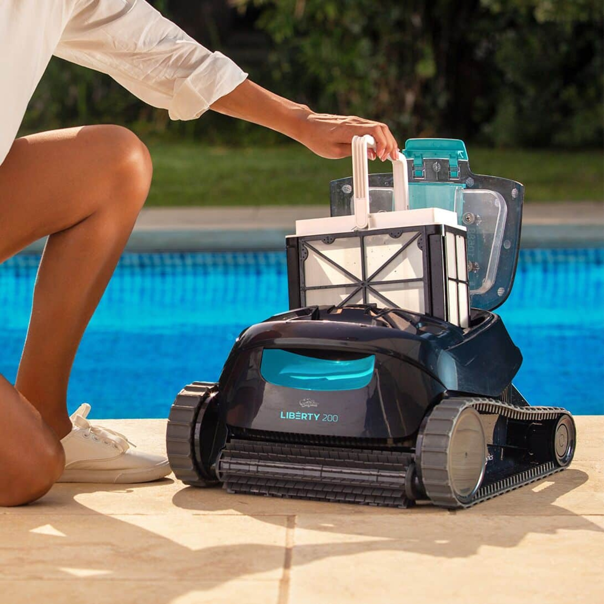 Persona abriendo un robot limpiador de piscinas. El robot de la piscina es negro y turquesa. Hay una piscina en el fondo.