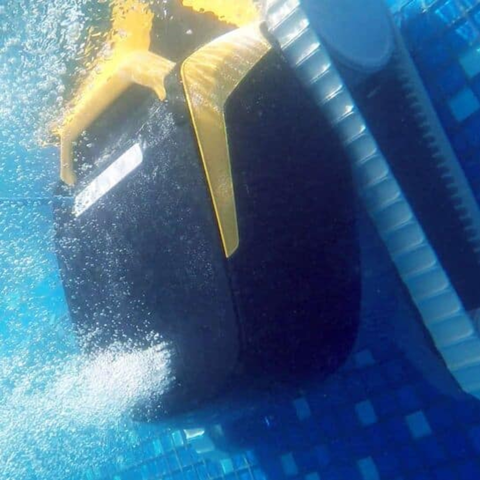 Un robot limpiador de piscinas bajo el agua, en primer plano. La máquina es negra y amarilla.