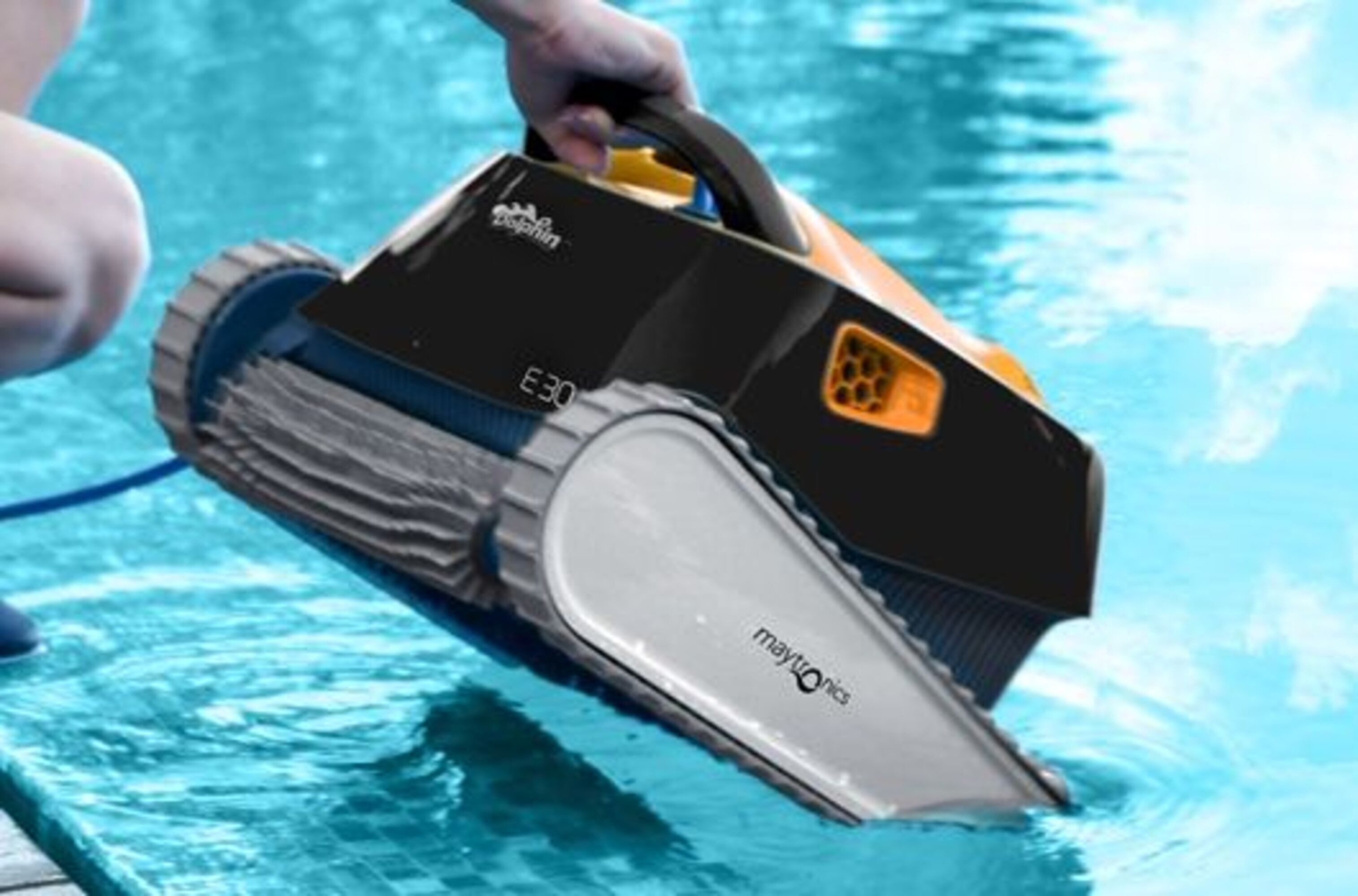 Una persona sosteniendo un limpiador de piscina parcialmente sumergido en agua. La máquina es negra y amarilla.