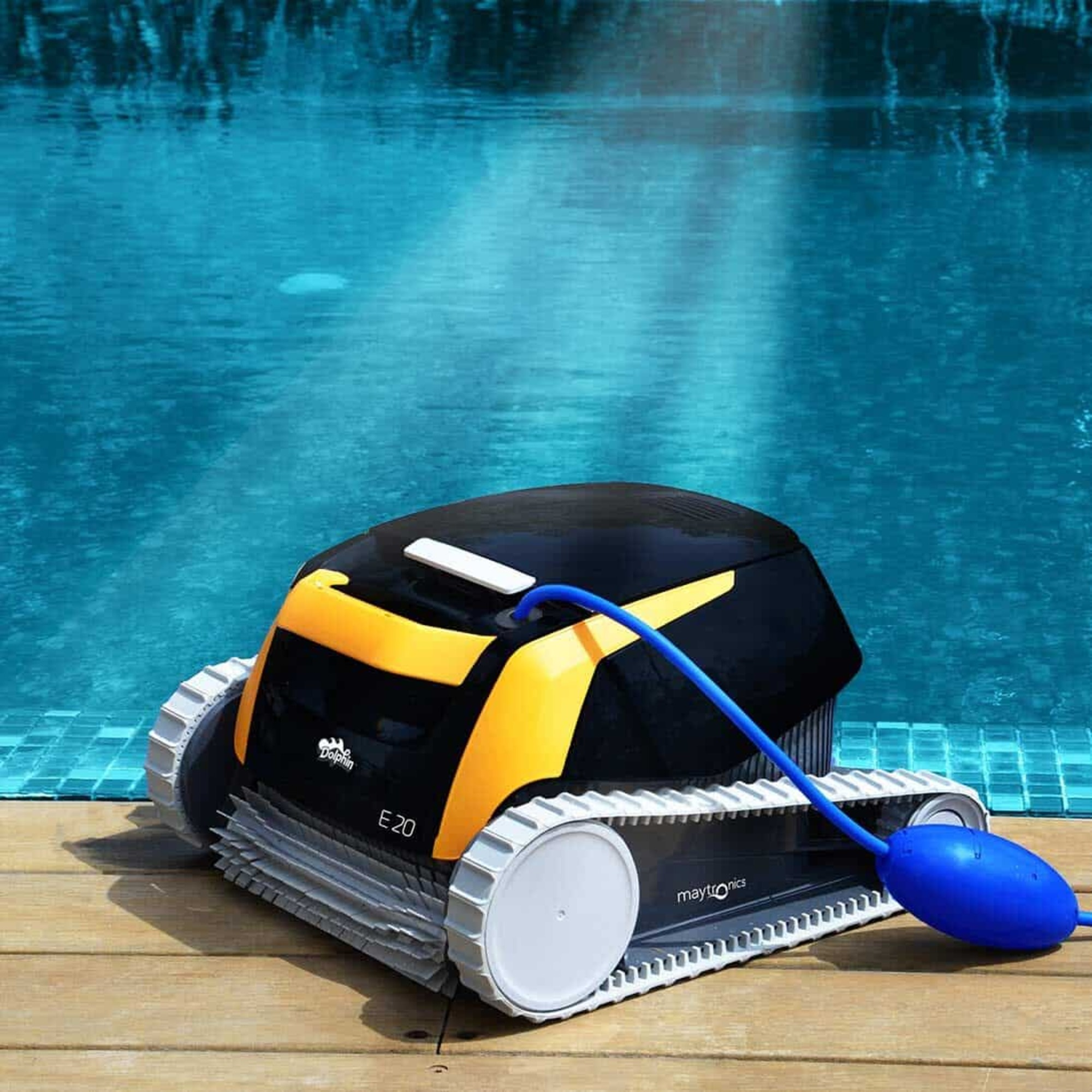 Limpiador de piscinas robótico en la piscina. Es negro y amarillo con orugas y una manguera. El agua es azul y quieta.