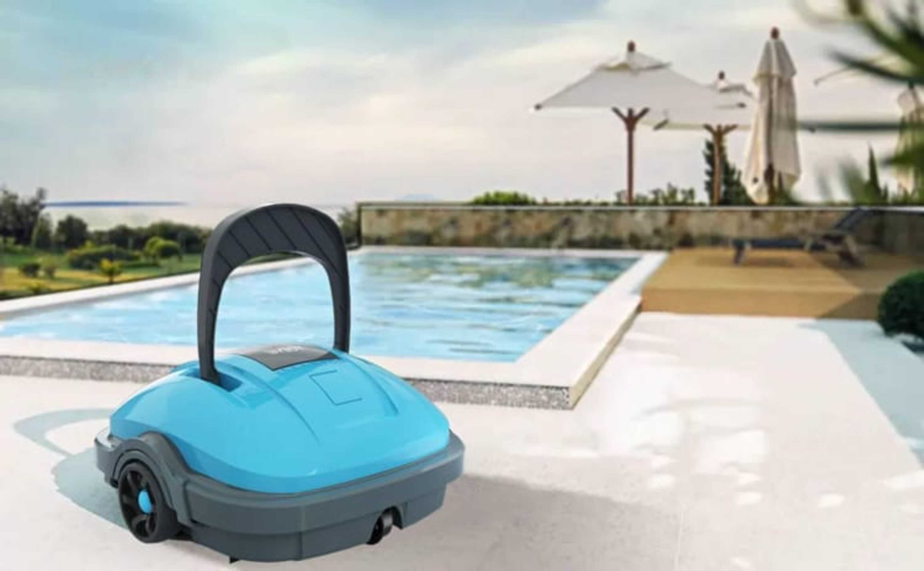 Un limpiador de piscinas está cerca de una piscina. La piscina está rodeada por una terraza y hay sombrillas en el fondo.