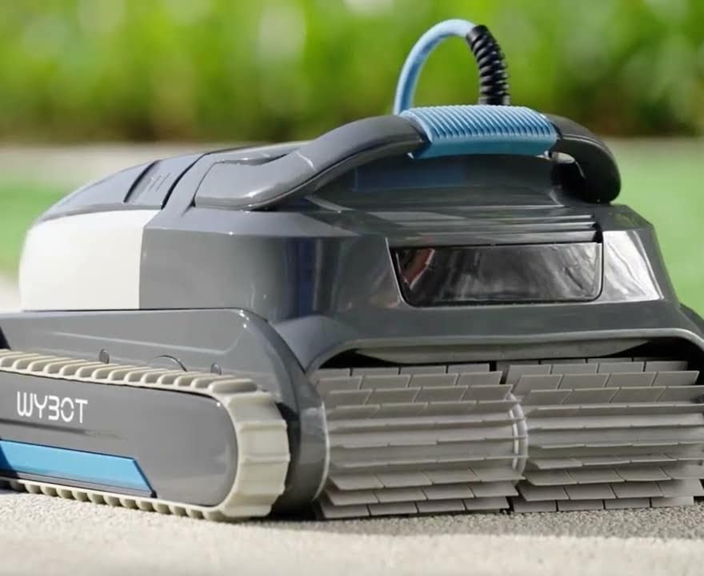 Un robot limpiador de piscinas de cerca. Tiene detalles grises y azules y un logotipo 'WYBOT'. Está en una cubierta.