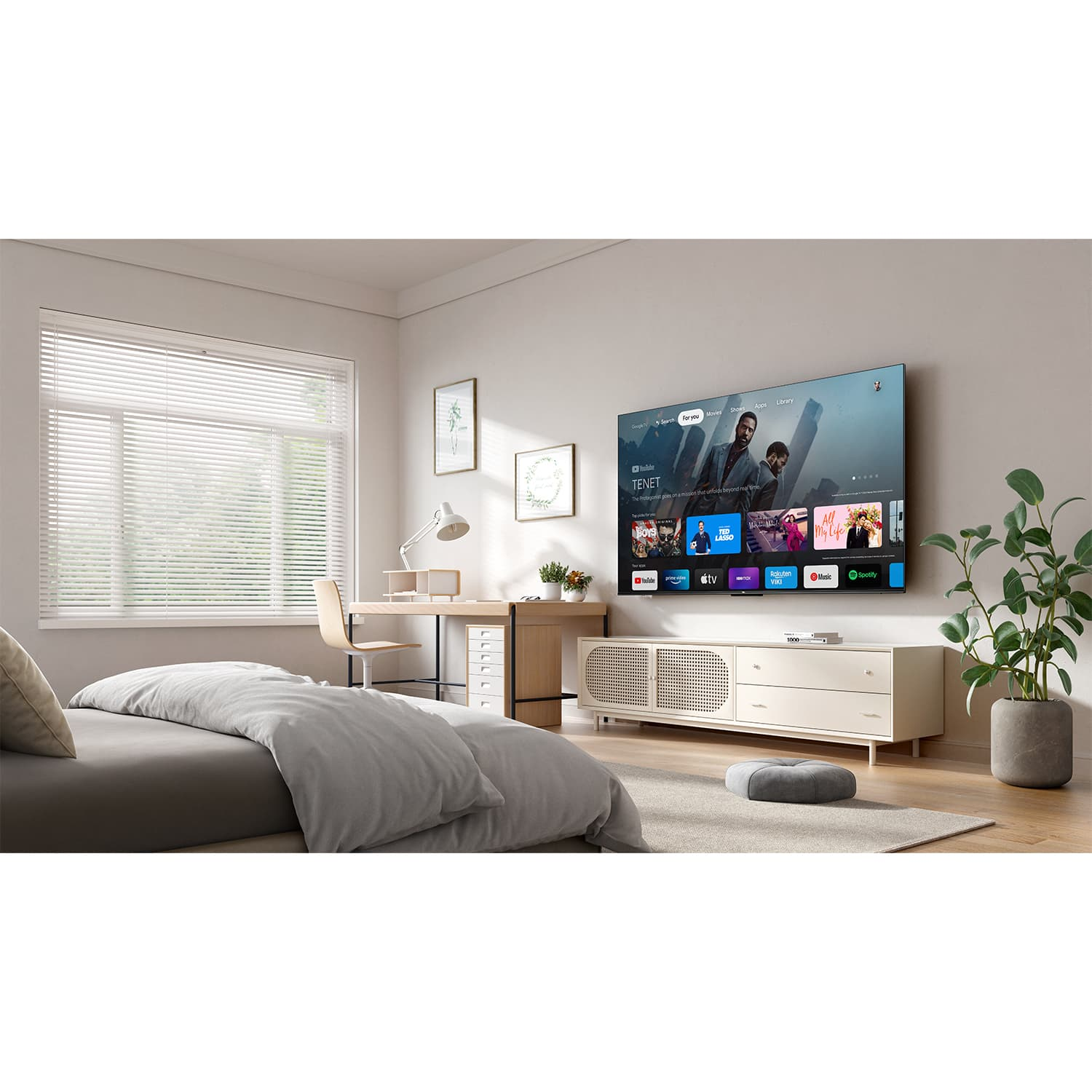Schlafzimmer mit Bett, Fernseher, Schreibtisch und Pflanze. Fenster mit Jalousien sichtbar.