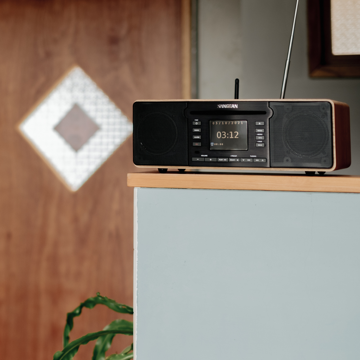 Una radio in legno su una superficie blu. L'orologio mostra 03:12 e la data 05/10/2023.