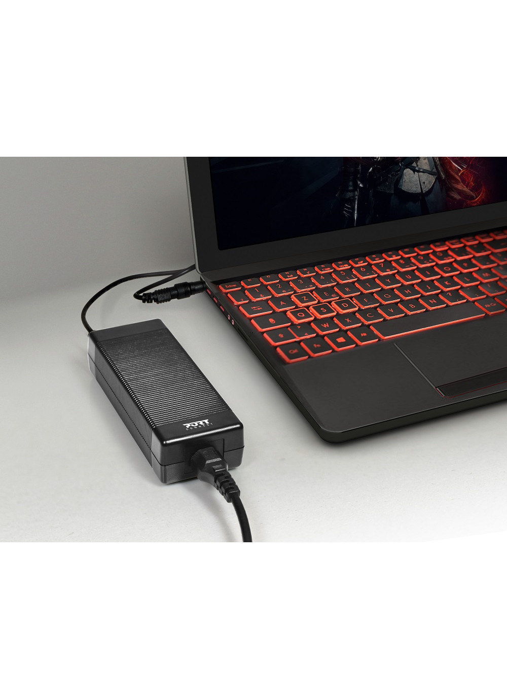 Adattatore di alimentazione nero collegato a un laptop con tastiera retroilluminata rossa.