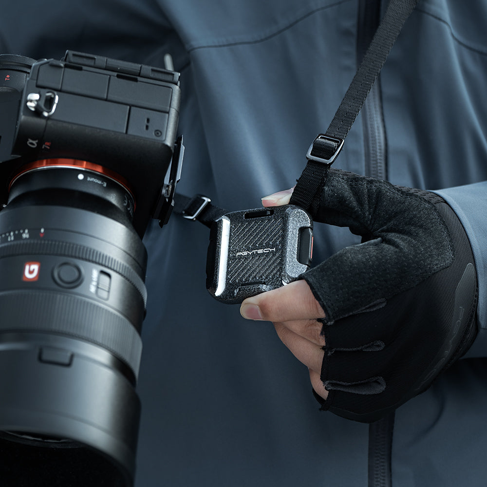 Un accessorio per fotocamera attaccato a una fotocamera e a un cinturino. Una mano con un guanto nero tiene l'accessorio.