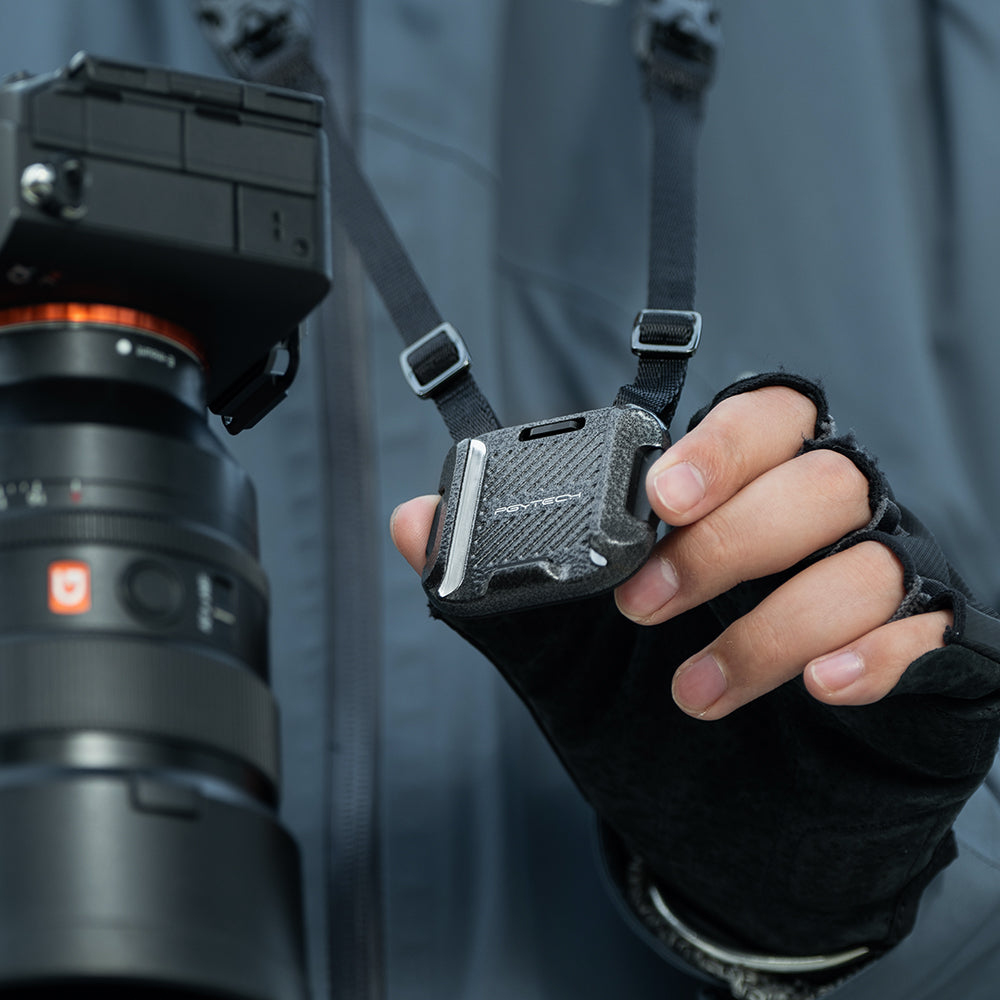 Un accessorio per fotocamera attaccato a una fotocamera e a un cinturino. L'accessorio è tenuto da una mano guantata.