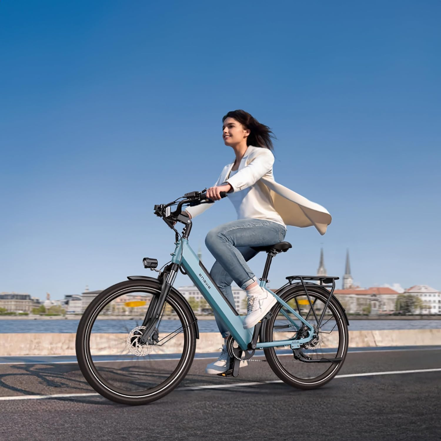 Frau fährt auf einer Straße ein Elektrofahrrad, blauer Himmel, Stadt im Hintergrund.