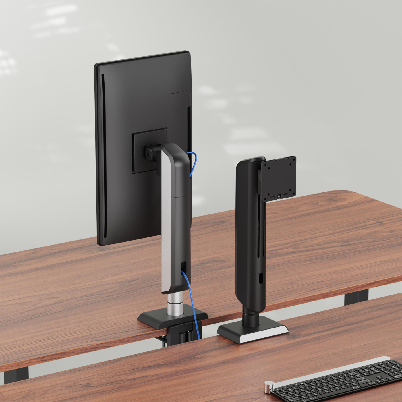 Twee monitorarmen op een houten bureau. Eén houdt een monitor vast, de andere is leeg. Een toetsenbord staat op de voorgrond.