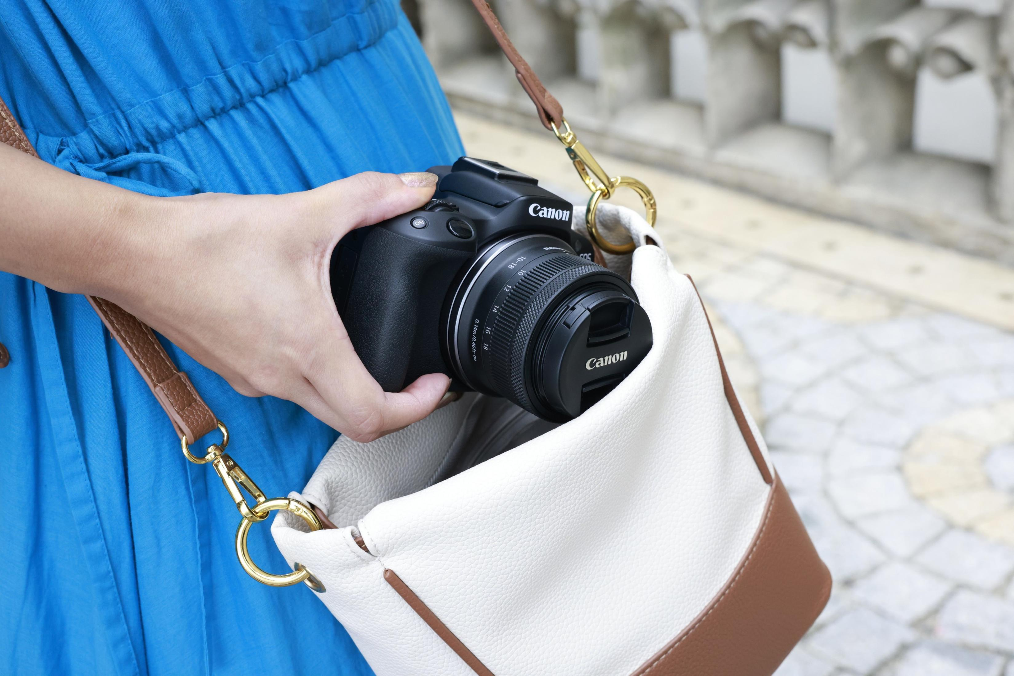 Die Hand einer Person, die eine schwarze Canon-Kamera hält, in einer weißen und braunen Handtasche.