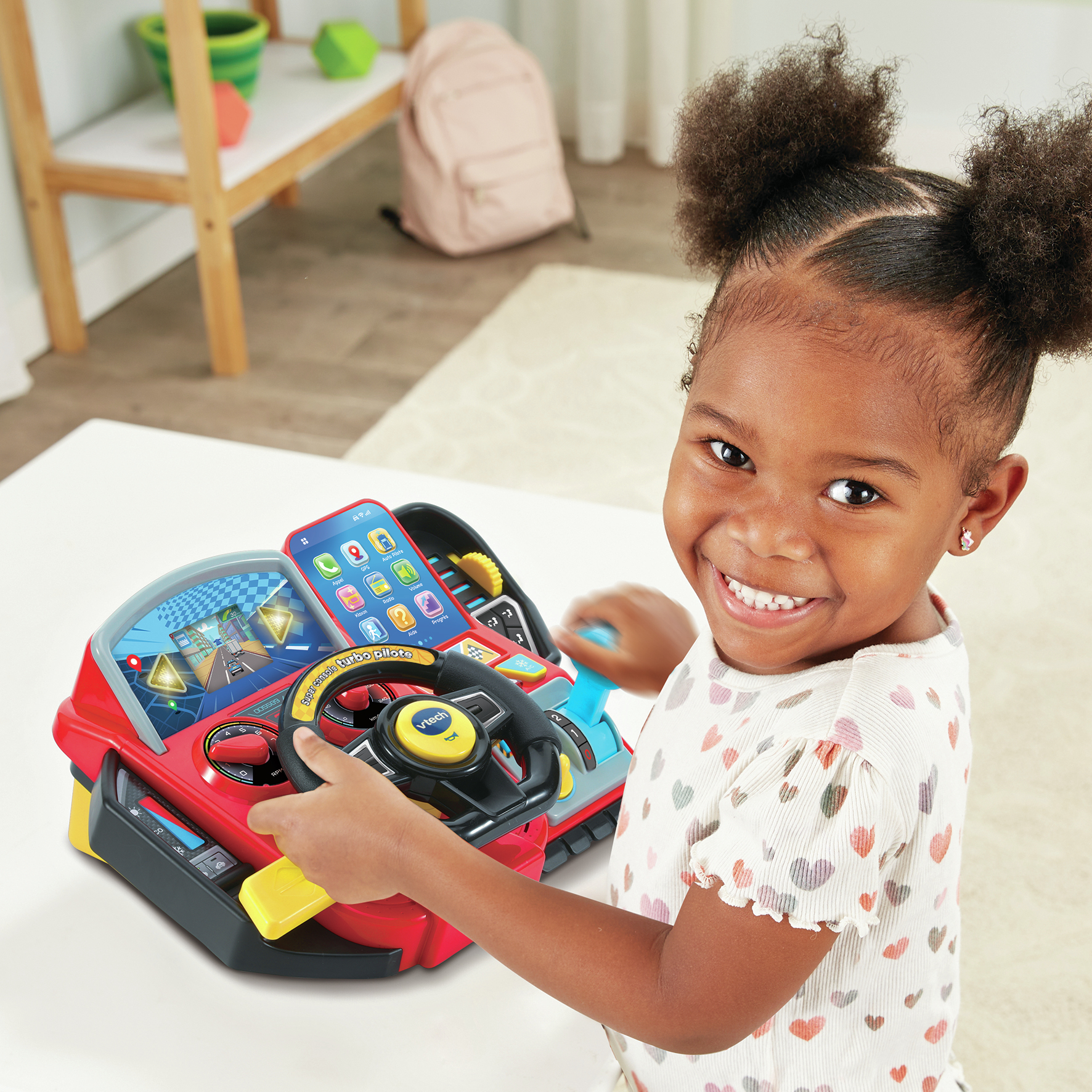 Una bambina sorridente gioca con una console per auto giocattolo rossa, guardando la fotocamera.